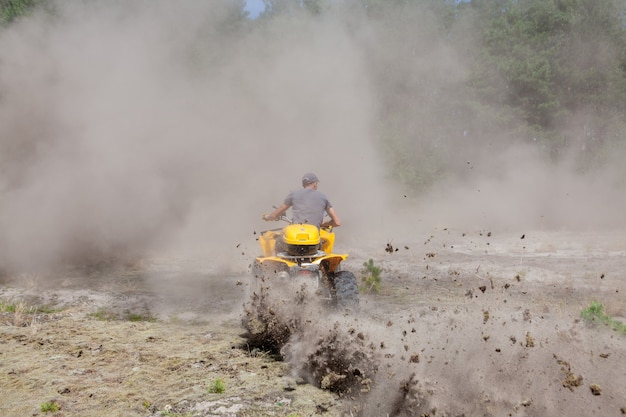 砂浜の森で黄色の四輪バギーATV全地形車両に乗る男。