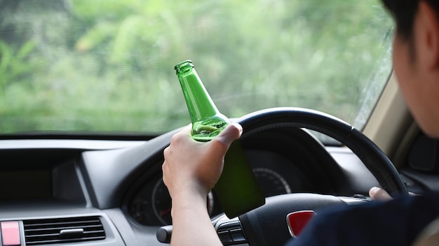 Man rijdt auto terwijl hij een flesje bier vasthoudt Rijden onder invloed