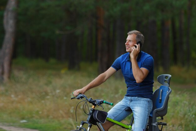 Man rijdt op de fiets in dennenbos en praten via de telefoon, sport vrije tijd. Fietser wandeling in park, actieve gezonde levensstijl