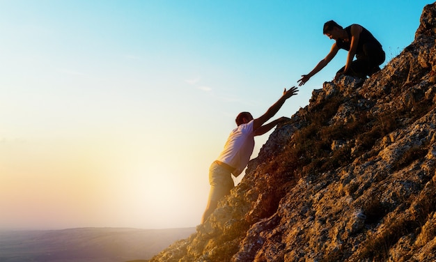 man rock climbing with another man helping