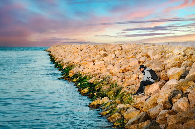 Man on rocky pier at sunset