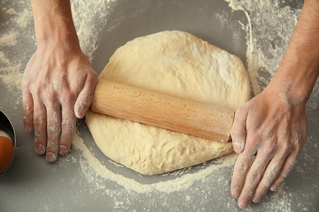 Man rolling out dough on kitchen table close up