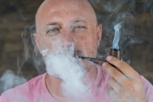 Foto man rookpijp. portret van een man van middelbare leeftijd binnenshuis. slechte gewoonten, verslaving. ongezond levensstijlconcept. detailopname