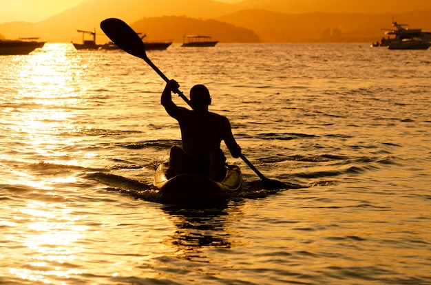 夕焼けに対して海で夕暮れ時に漕ぐ男