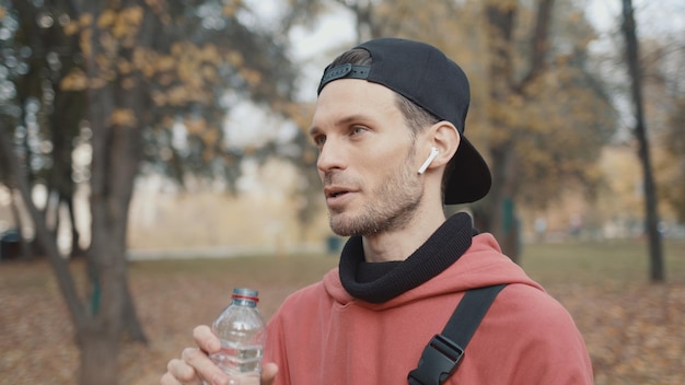 Man runner in red hoodie having a sips of water in city park slow motion