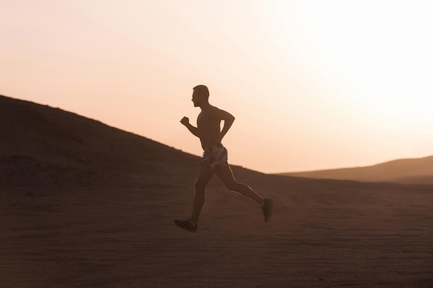 Бегущий человек бежит по дюнам на закате