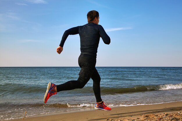 Man runner on the seashore in sports outfit. Cardio jogging