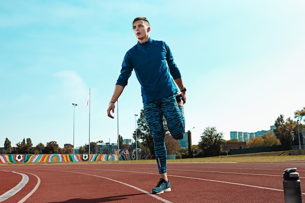 Corridore uomo che allunga le gambe preparandosi per l'allenamento di corsa sulle piste dello stadio facendo riscaldamento