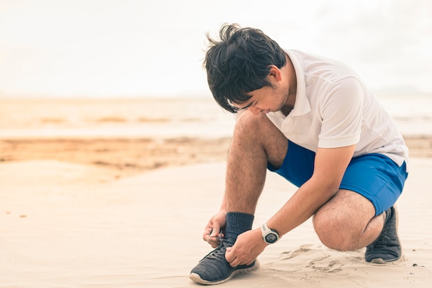 Foto corridore dell'uomo che lega i lacci delle scarpe pronti a funzionare sulla spiaggia