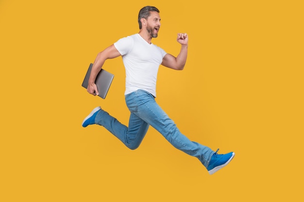 Man running with computer man hold laptop isolated on yellow background jumping man