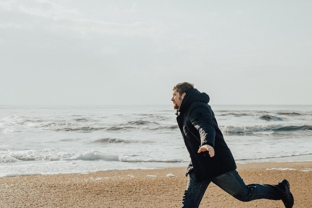 Мужчина бежит по берегу моря в зимний день Путешествия и походы