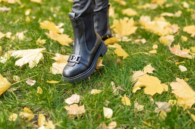 Мужской черный ботинок стоит в траве с желтыми листьями на земле.