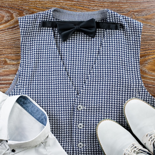 Man's classic clothes outfit flat lay with formal shirt, vest, bowtie, shoes.