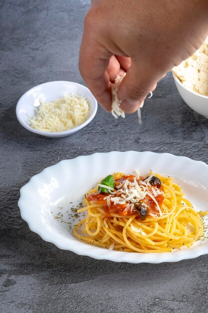 Man's hand adding parmesan cheese on a plate of italian pasta with amatriciana sauce. Ready to eat,