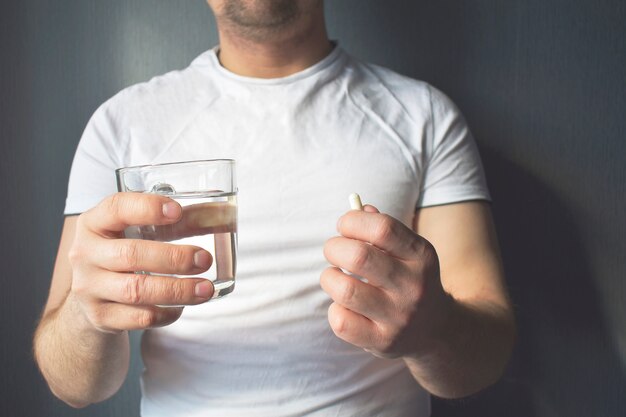 In the man's hand are medicinal tablets and a glass of water.