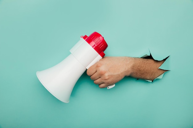 Man's hand arm hold megaphone isolated through torn blue background