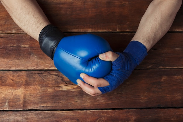 La mano dell'uomo in fasciature di pugilato tiene una mano in un guantone da pugile su un fondo di legno. gesto pronto. concetto di allenamento per allenamento o combattimento di boxe.