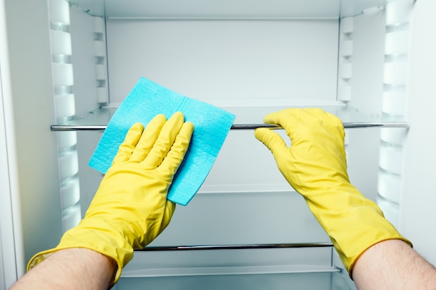 Man's hand cleaning white fridge with blue rag