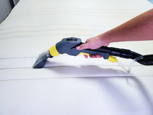 Man's hand cleans a modern white mattress with a professional cleaning agent