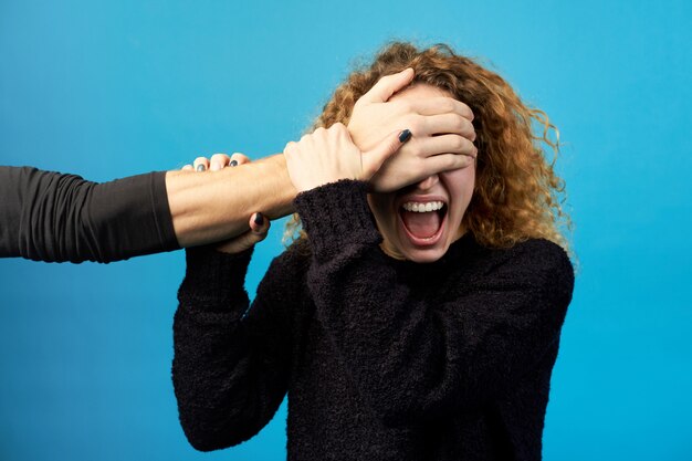 Man's hand closes eyes of young red-haired curly woman.