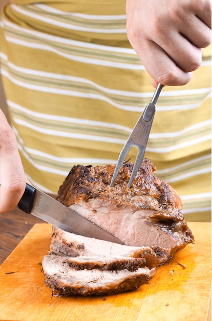 Man's hand cuts the baked meat with a knife on cutting board