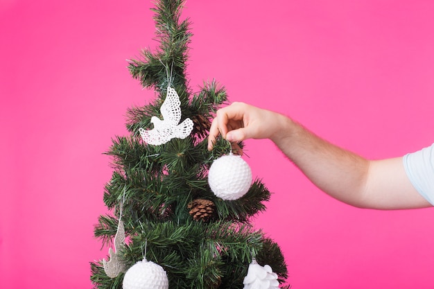 Man's hand decorating Christmas Tree on pink