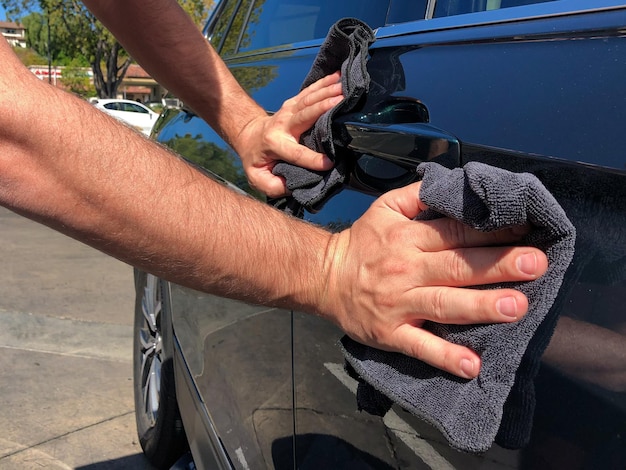 Man's hand die de auto schoonmaakt met een zwarte microvezeldoek. veeg het oppervlak van de auto met de hand af.