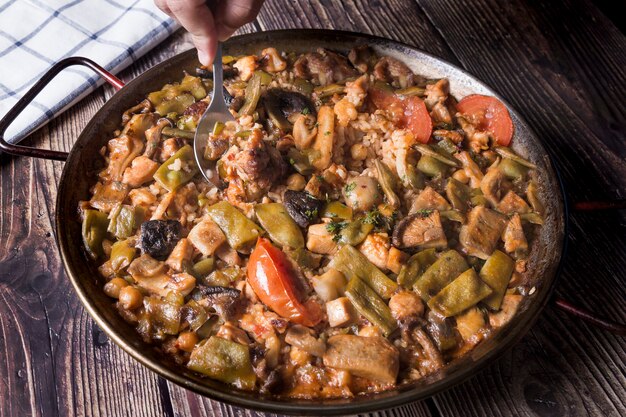 A man's hand, eating a vegetable paella with a spoon. Tasting a traditional Spanish meal.