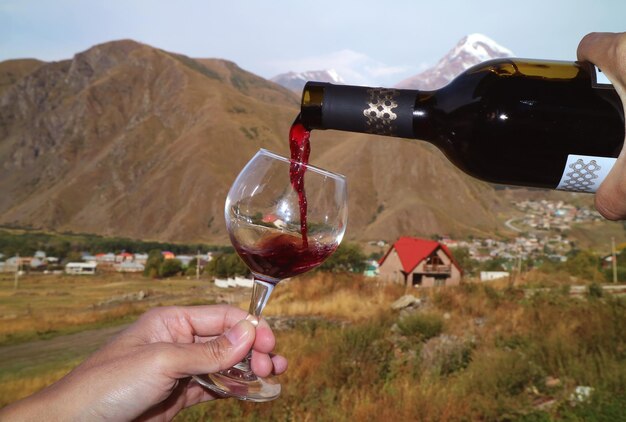 Man's hand gieten rode wijn uit de fles in wijnglas in het dorp mount kazbek