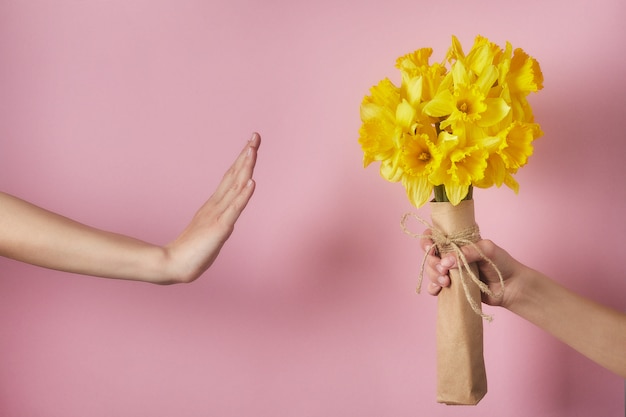 Man's hand gives bouquet of yellow narcissus flowers to girl and receives refusal