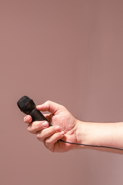 La mano di un uomo che tiene un microfono nero. concetto di comunicazione, interviste, dialoghi virtuali.