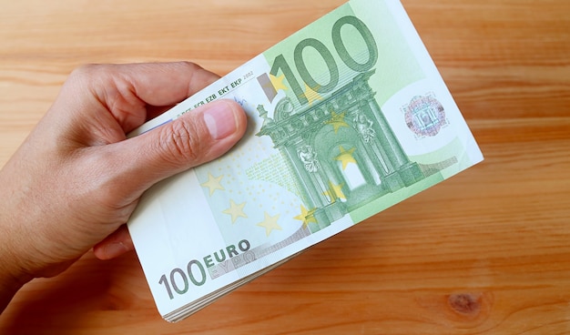 Man's Hand Holding bundel van 100 euro bankbiljetten op houten achtergrond