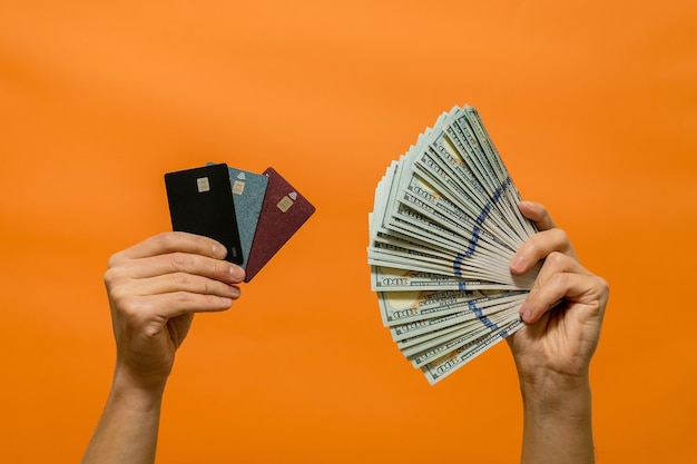 オレンジ色の背景に分離された現金とクレジット カードを持っている男の手