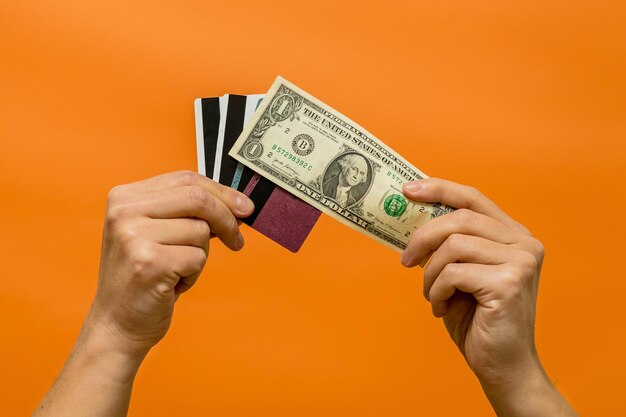 Man's hand holding cash and credit cards isolated on orange background