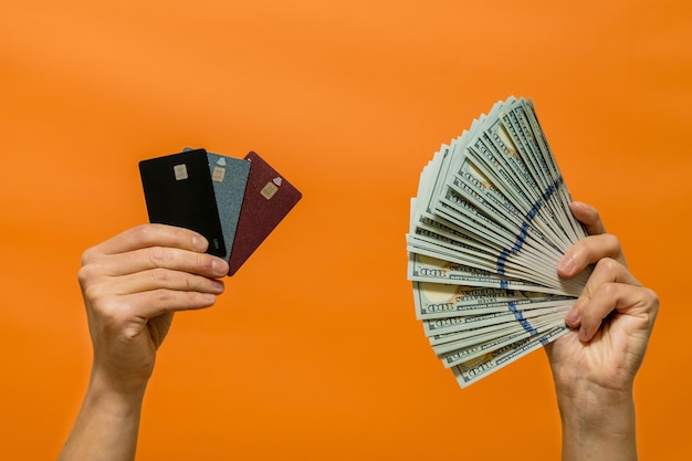 Мужская рука с наличными и кредитными картами на оранжевом фоне