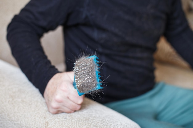 a man's hand holding the cat comb brush with gray fur.