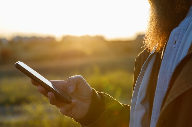 A man's hand holding a cell phone in the field at sunset