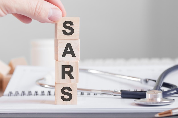 man's hand holding a cube with the letter S from the word SARS written on wooden cubes near a stethoscope on a paper background, medical concept