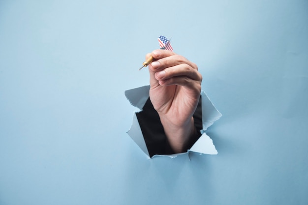 Man's hand holding a dart on a blue scene