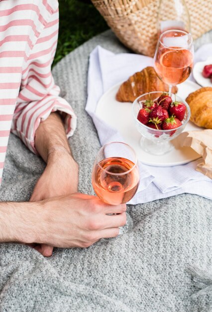 チーズとワインとバラのワインの夏のピクニックのグラスを持っている男の手