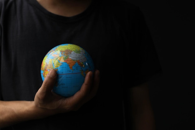 Man's hand holding a globe on a black background with copy space. Earth day concept with low key  