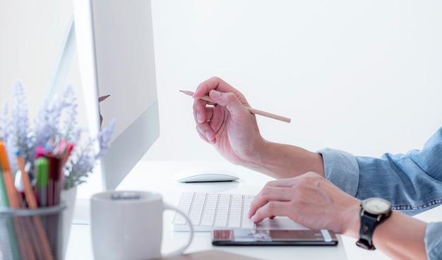 Man's hand holding pencil pointing on computer screen.