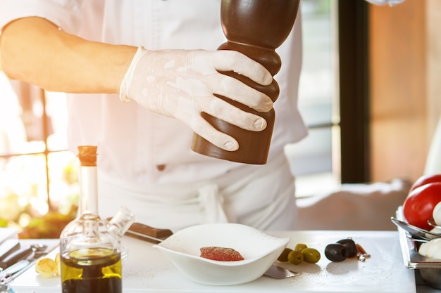 Man&#39;s hand holding pepper dispenser. Cooking board with food ingredients. Putting spice on raw tuna. Chef preparing breakfast.