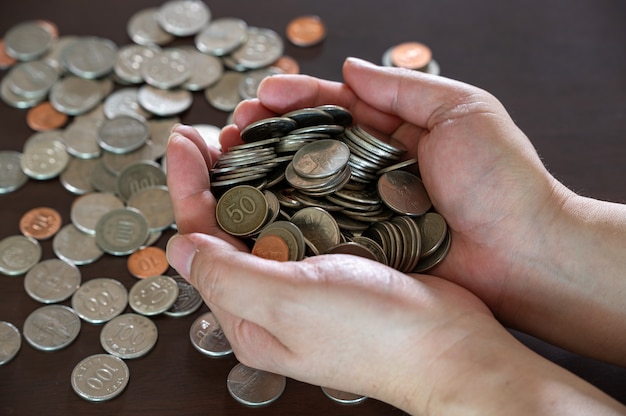 A man's hand holding a pile of coins on a wooden table.