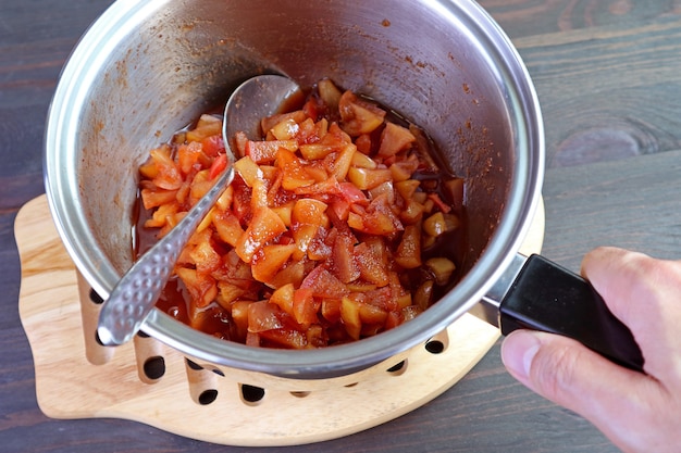 Man's hand holding a pot of fresh cooked caramelized homemade apple compote