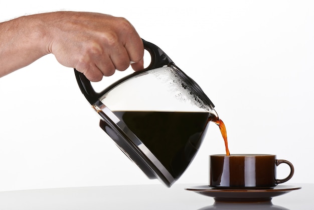 Photo man's hand holding and pouring coffee into a brown cup