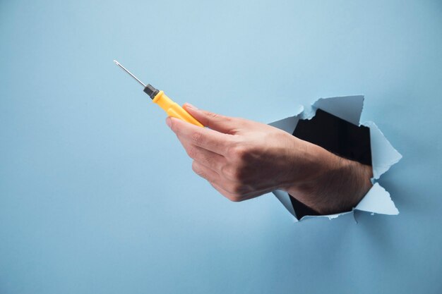 Man's hand holding a screwdriver on a blue scene