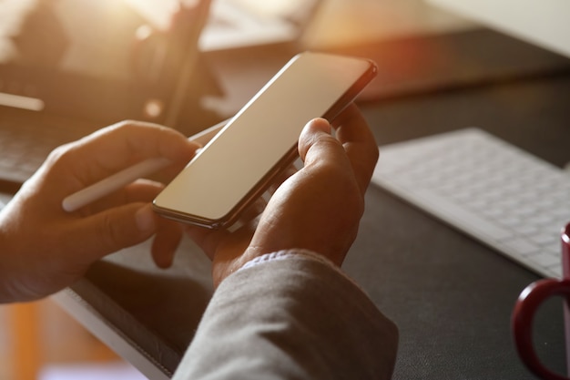 Man's hand holding and using mobile phone on workspace in office