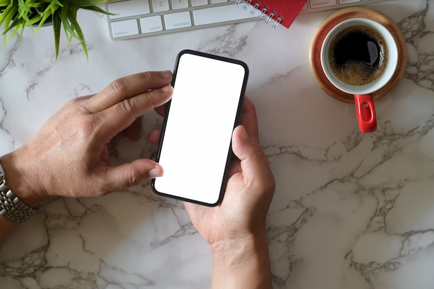 La mano dell'uomo che tiene telefono cellulare bianco sullo scrittorio di marmo