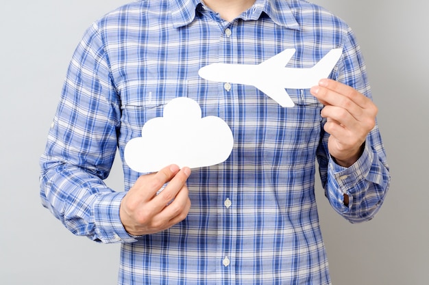 Man's hand holding white paper model of plane and cloud